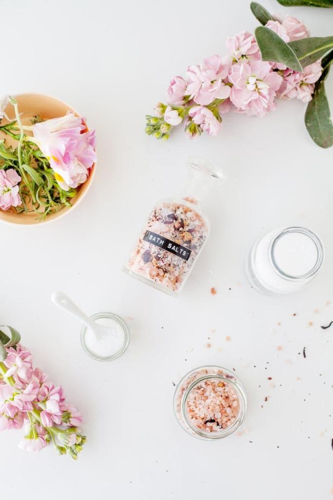 set of jars of bath salts composed with gentle matthiola incana flowers sit ready for a floral bath as a Beltane ritual