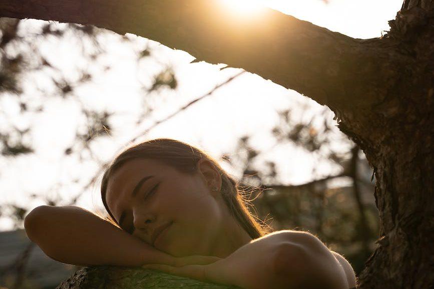 young woman resting her head on a tree branch, considering ancient solstice rituals and global solstice traditions for celebrating summer solstice
