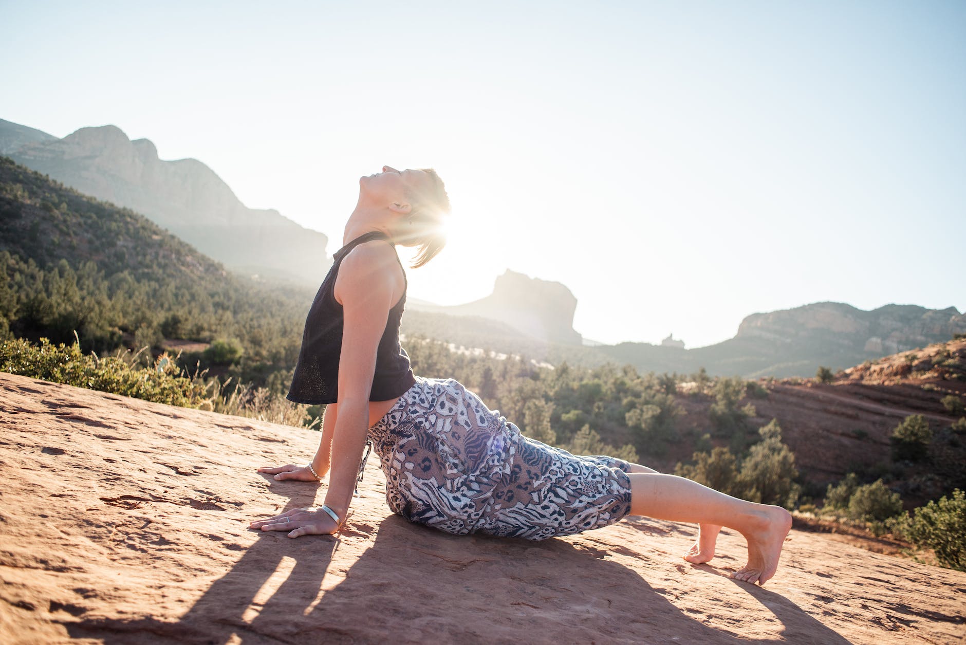 woman doing bhujangasana on sunlit cliff, summer solstice sun salutations and celebrating Litha with solar energy alignment