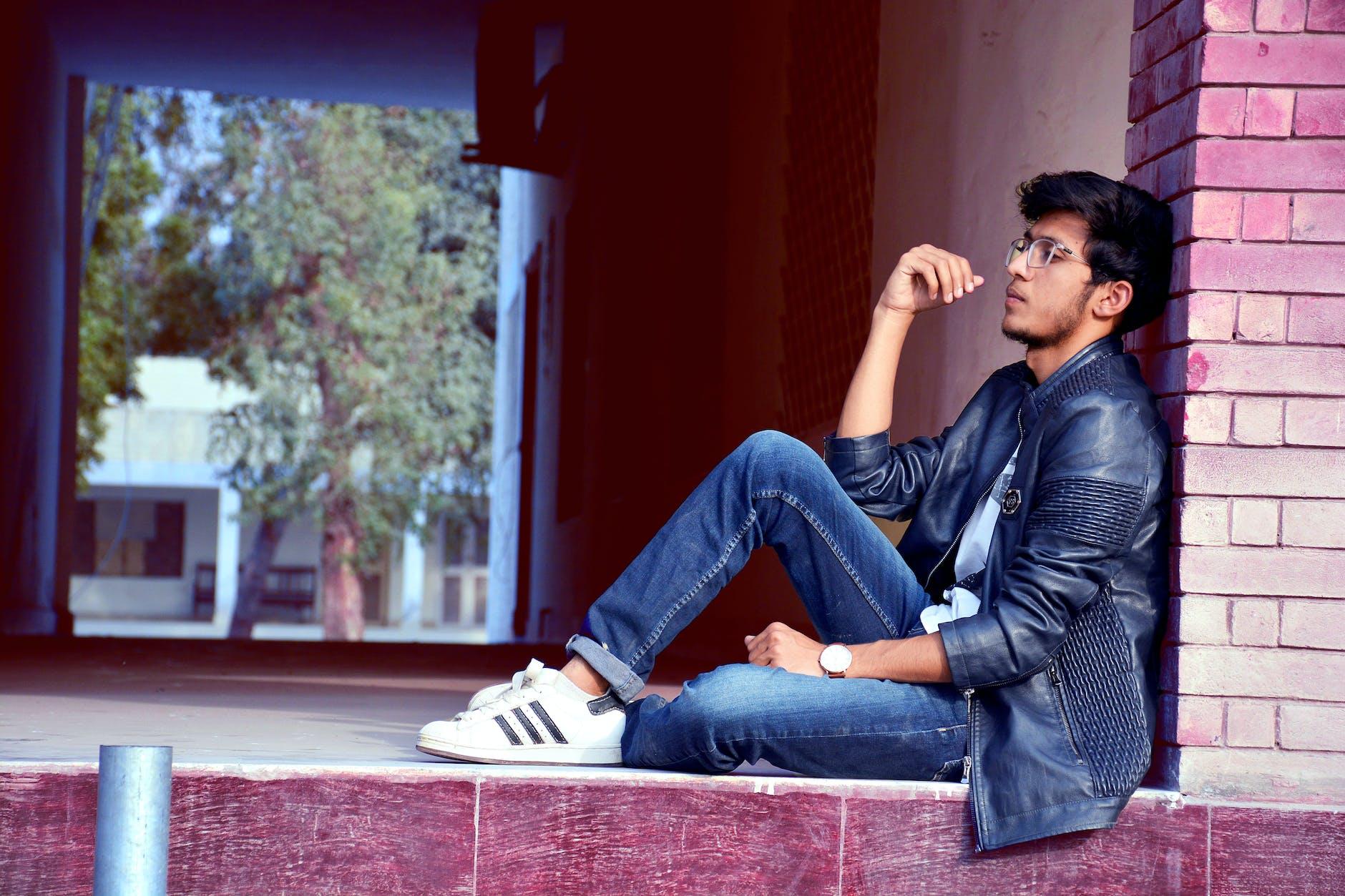 man wearing black leather jacket and blue jeans sitting on floor, illustrating meditation for stress relief in the moment by using mindfulness techniques