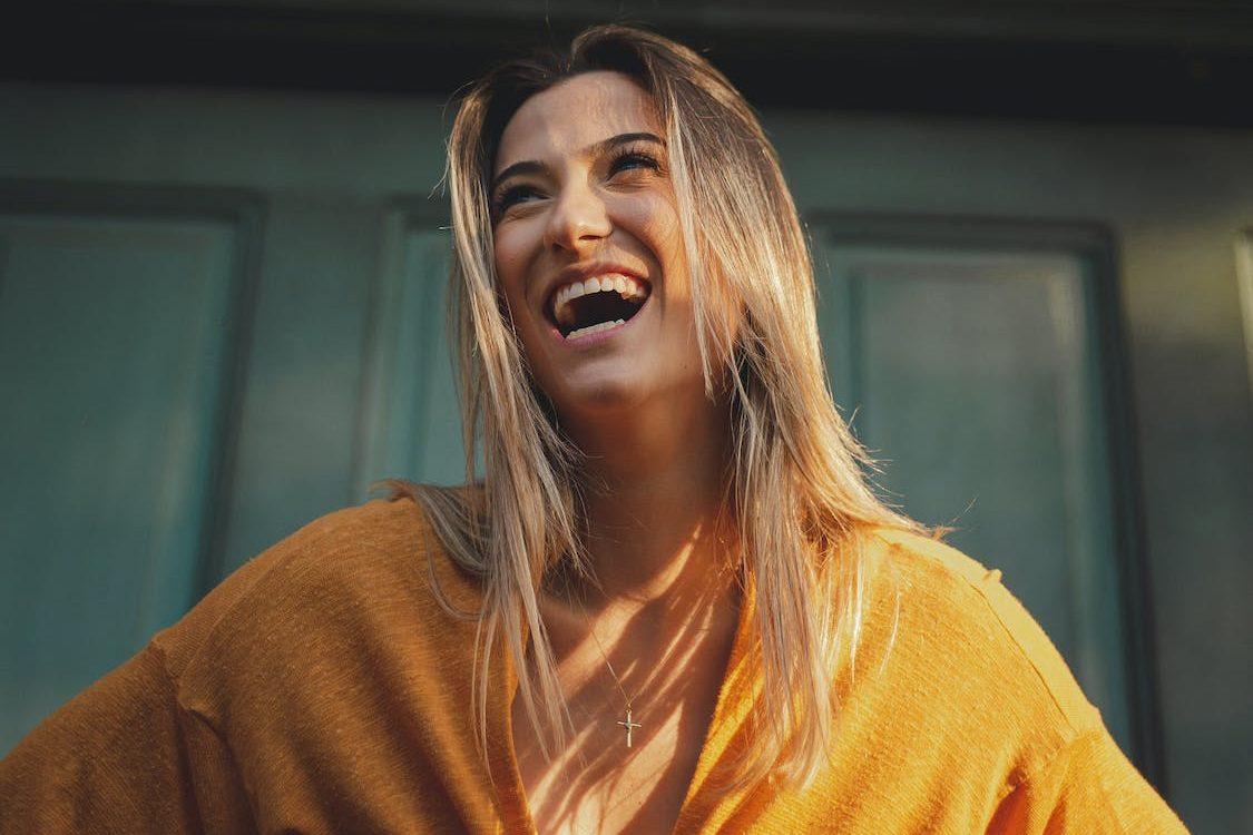 photo of a laughing woman wearing a yellow blouse, smiling, illustrating the power of meditation for stress relief