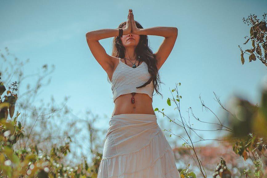 woman in meditation in white tank crop top on grassy field