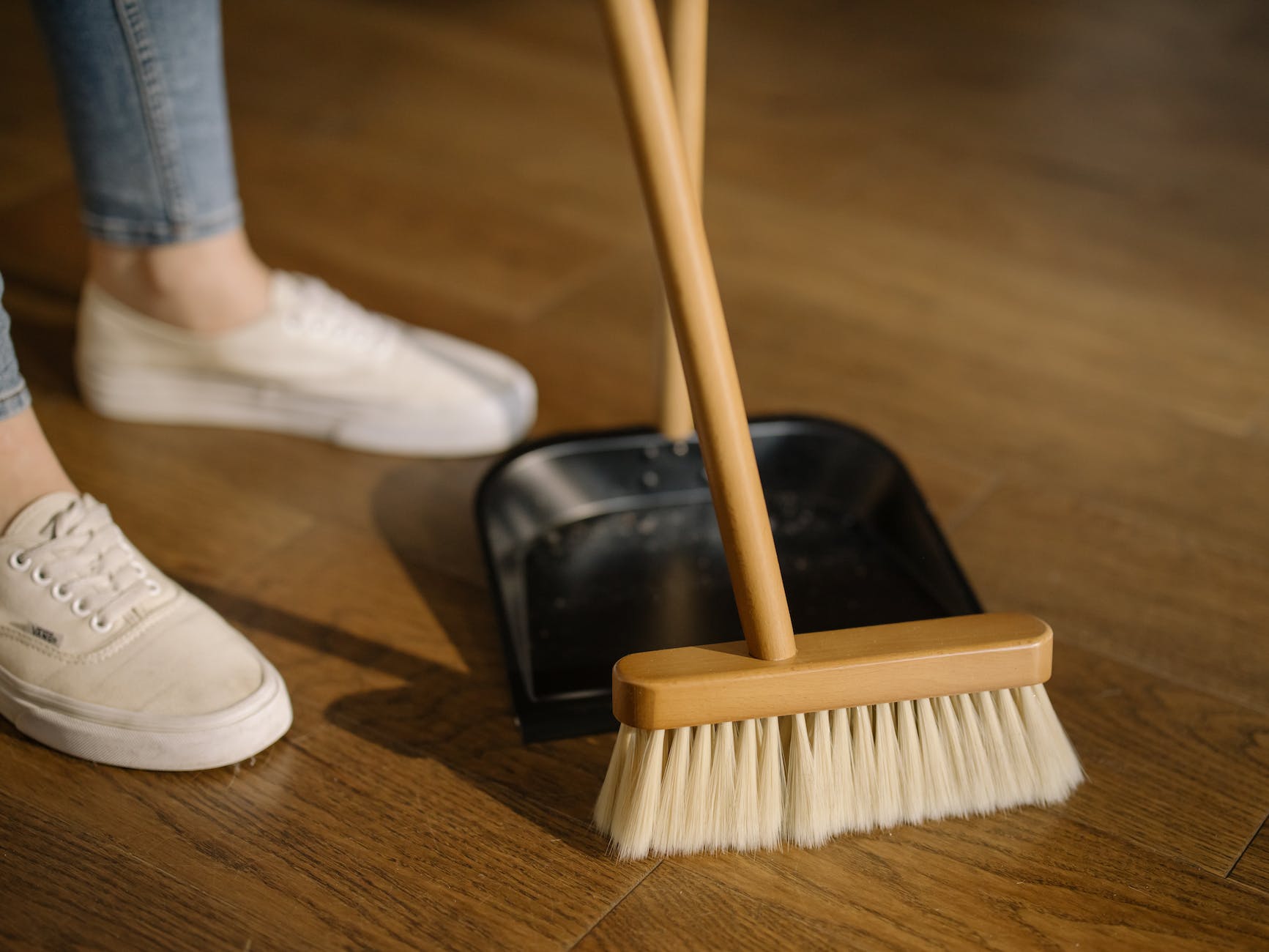 person wearing white pants and white socks standing beside brown broom, illustrating preparing for a daily meditation routine