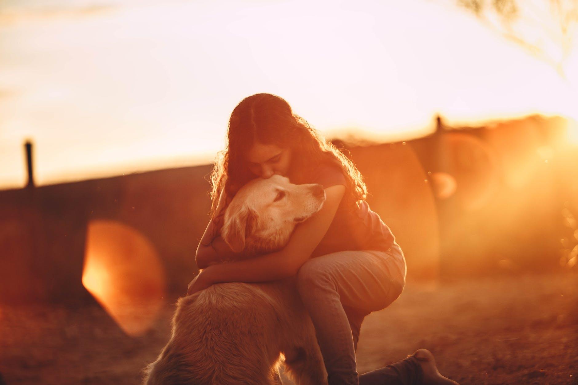 young woman hugging and kissing golden retriever dog in open air at sunset, practicing mindful self-compassion