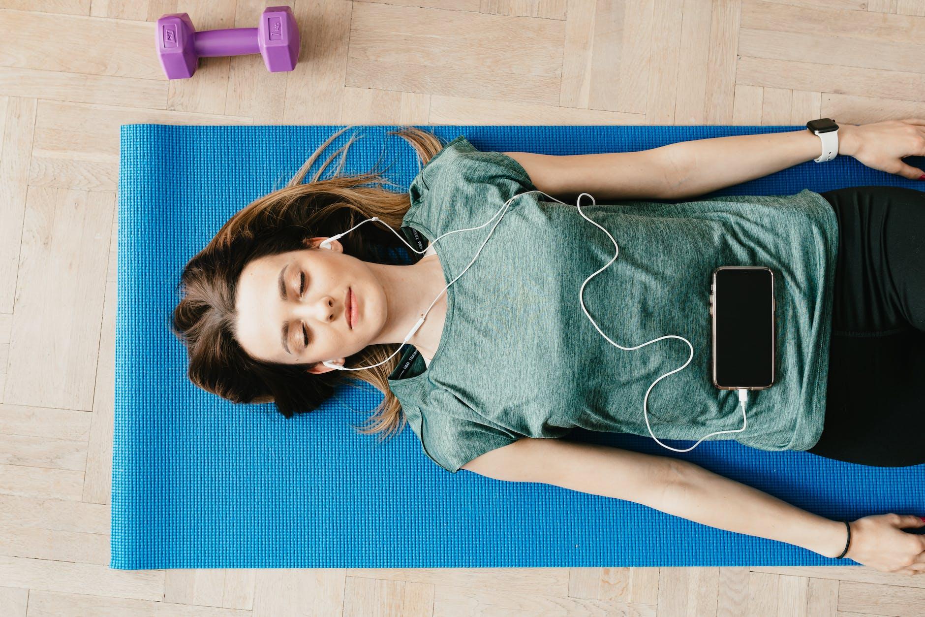 peaceful woman in earphones resting in shavasana pose for meditation at home