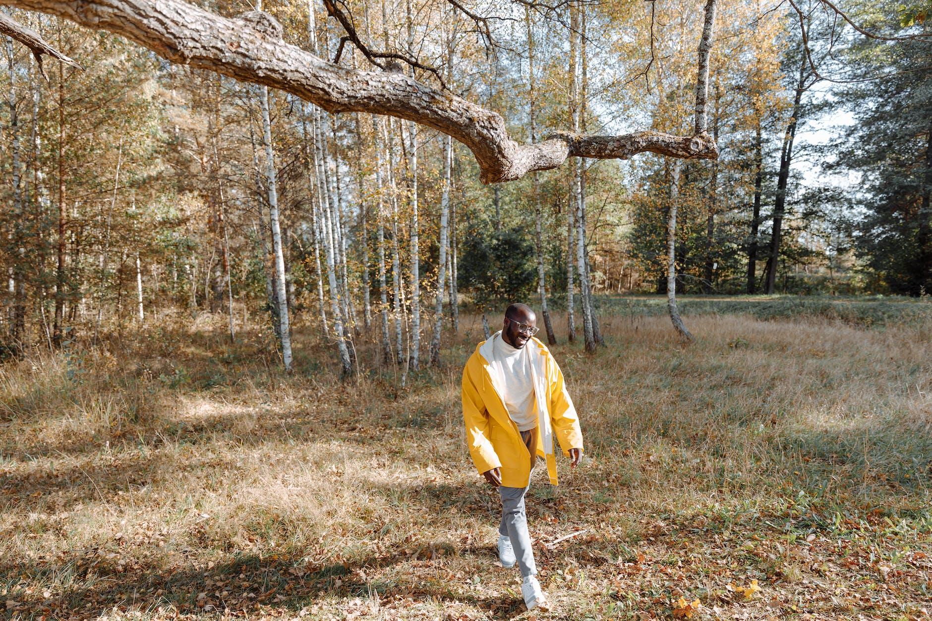 man in yellow long sleeve jacket and denim pants walking on a grass field