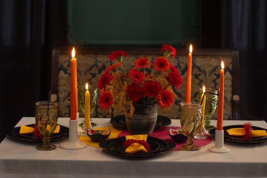 photograph of a table with candles and red flowers for Lughnasadh, first harvest, abundance festivals, to celebrate harvest and honor seasonal traditions
