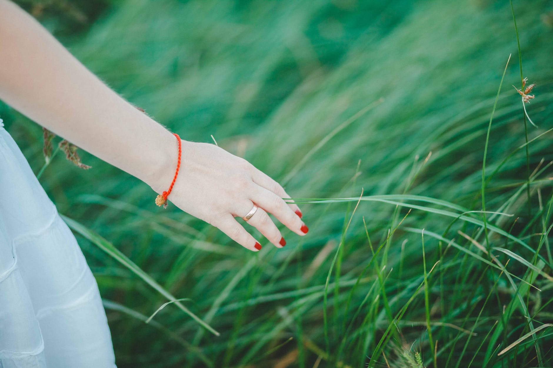 woman wearing white skirt orange bracelet and red manicure beside green grass