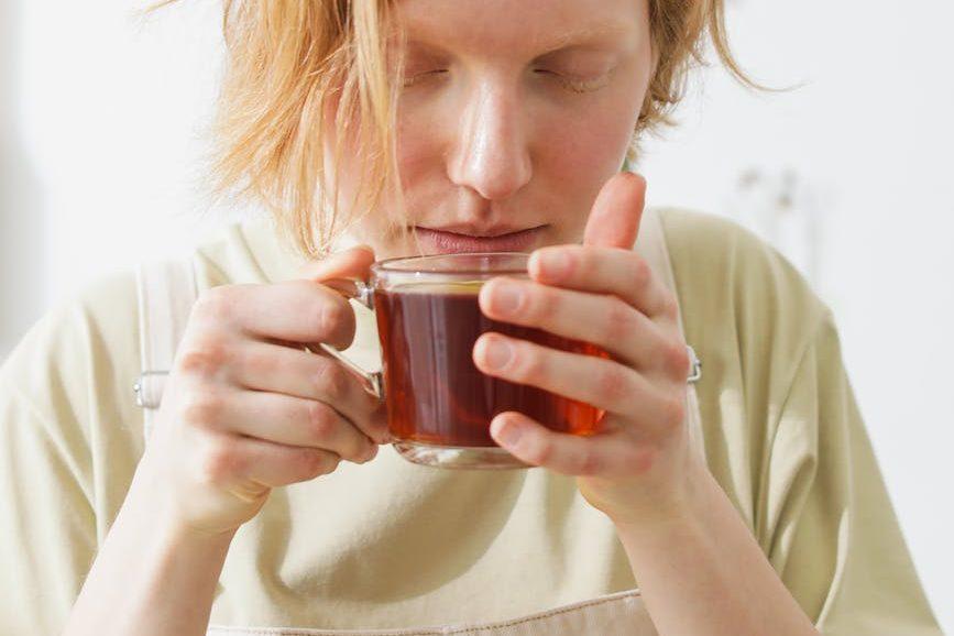blonde female holding a cup of tea, breathing deeply to illustrate the sensory engagement meditation technique