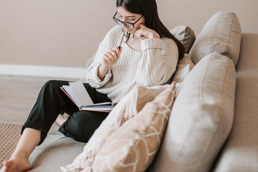 thoughtful young female freelancer reading diary at home