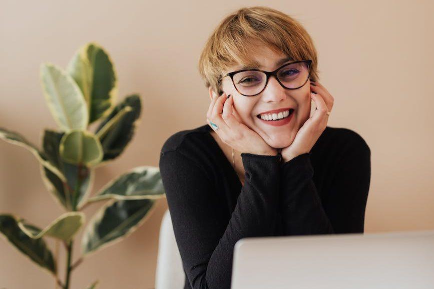 cheerful woman smiling while sitting at table with laptop