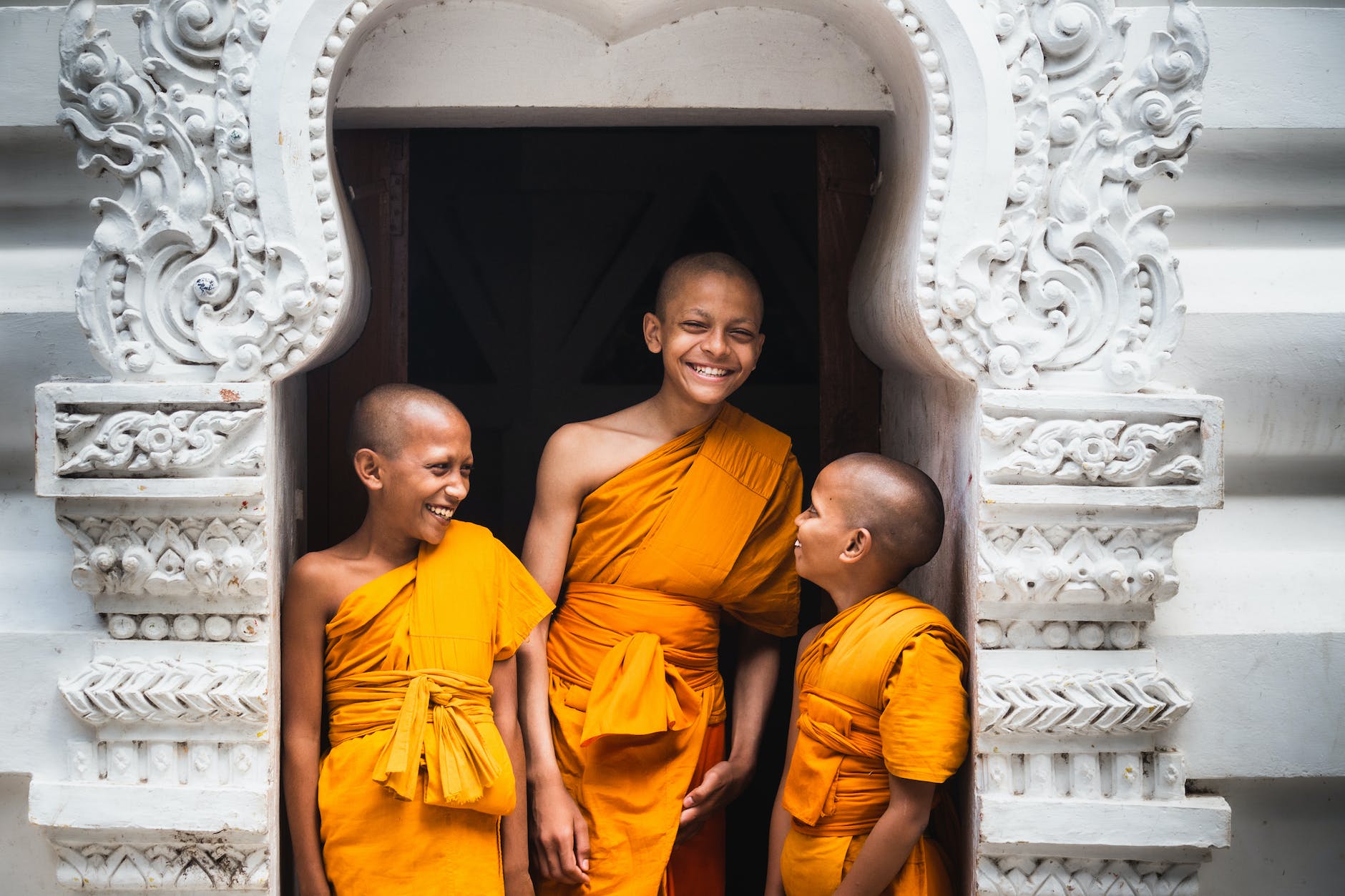 three young and smiling buddhist monks standing on doorway