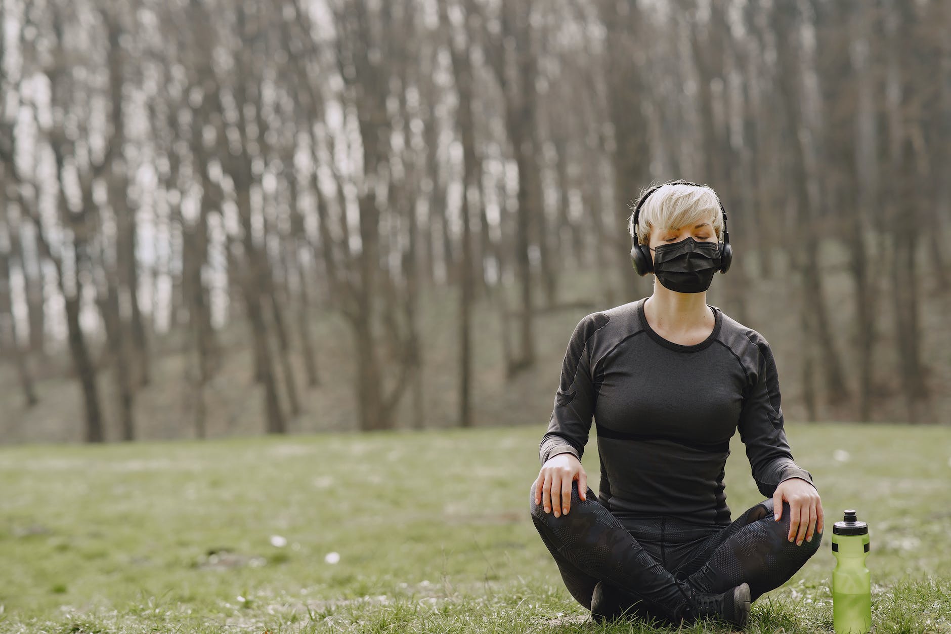 sportswoman in mask sitting in lotus pose in park