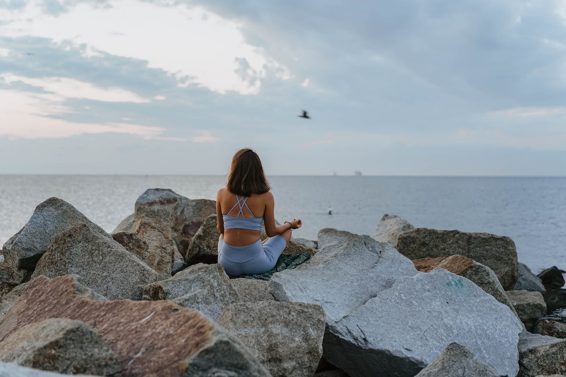 woman in blue sportswear meditating on rocks near sea