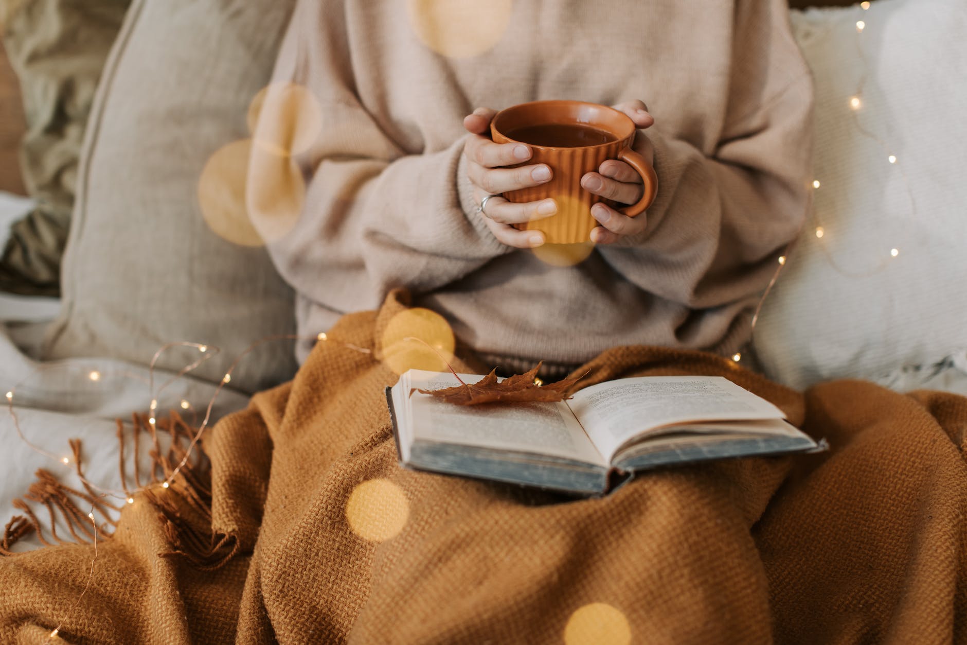 person in beige sweater holding a cup of warm beverage, illustrating: a feast ritual, sacred eating, Autumn Equinox, harvest celebration, and seasonal food