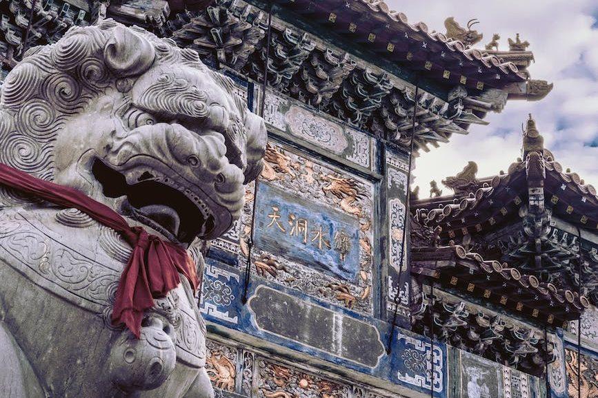 sculpture of chinese guardian lion in front of the buddhist temple gate