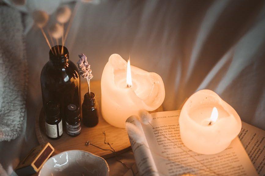 lighted candle on white book beside black glass bottle