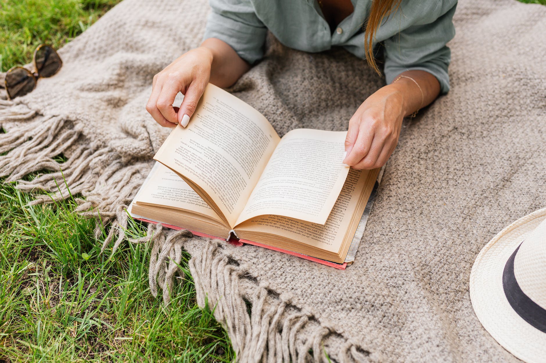 close up of woman on blanket reading book outdoors