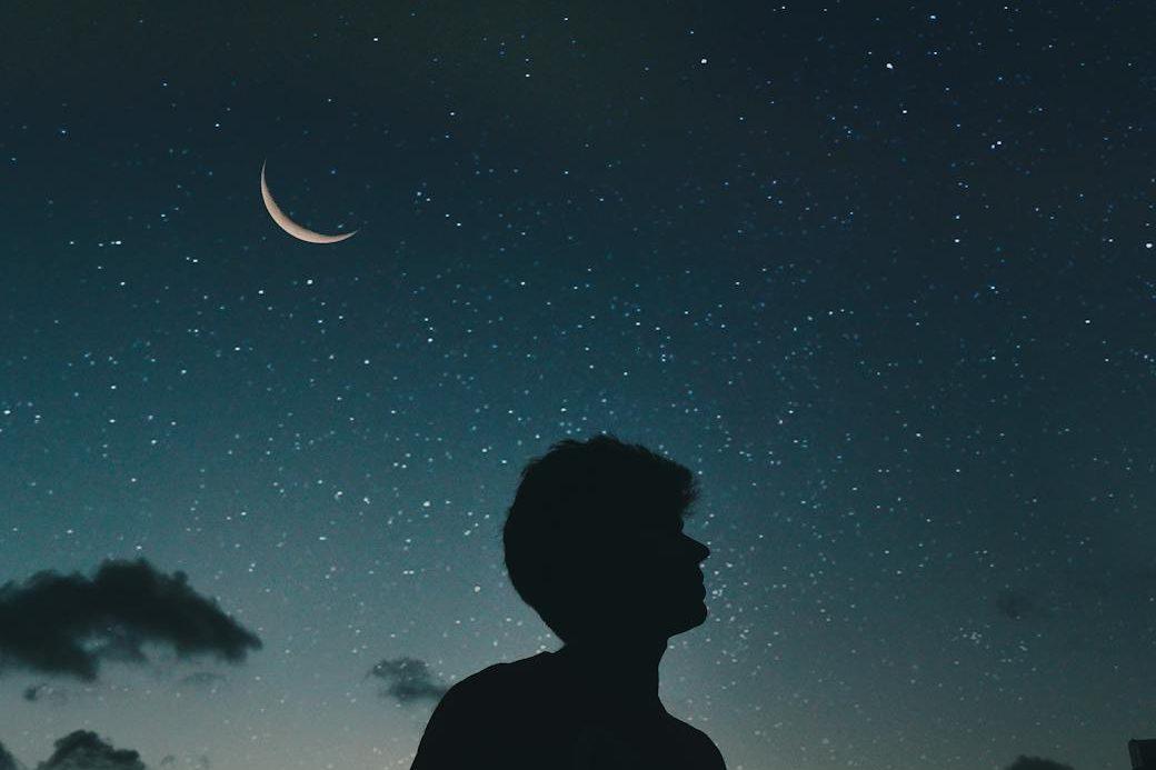 silhouette of man during nighttime before a crescent moon, showing: moon effects on humans, lunar rhythms, lunar phases and emotions, moon influence science, and moon biological rhythms