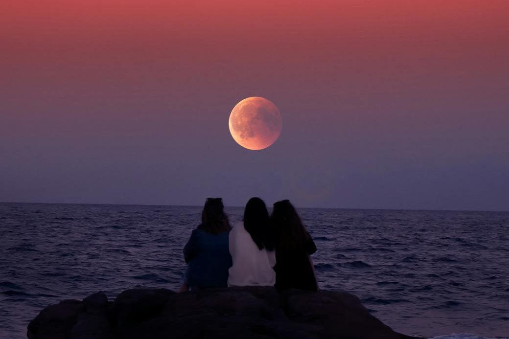 women sitting on rock infront of ocean, illustrating lunar cycle, moon rituals, moon phases meaning, lunar wisdom, and working with the moon