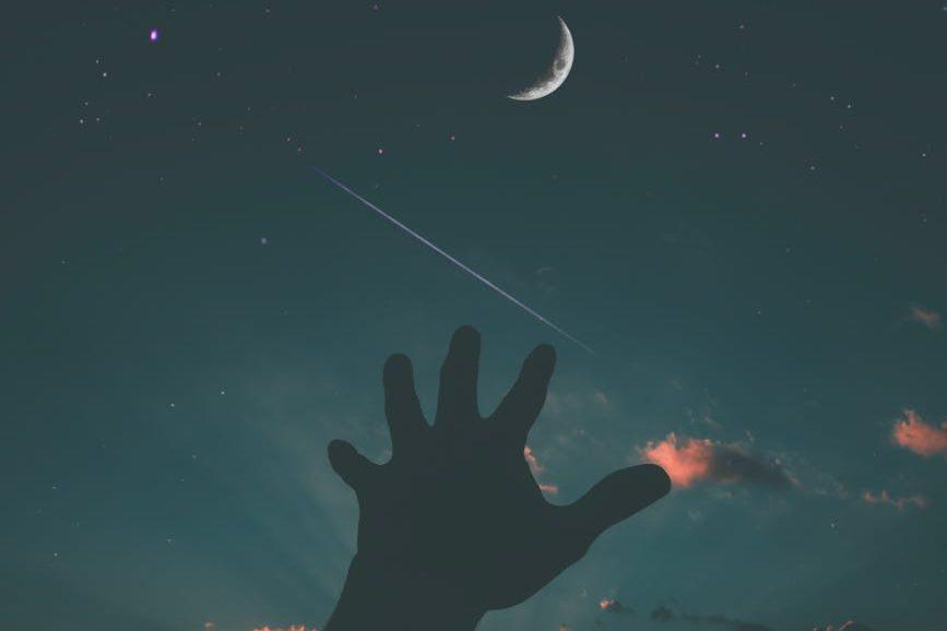 person hand and crescent moon, illustrating: moon rituals, lunar traditions, modern moon practices, lunar guidance, and intention setting rituals