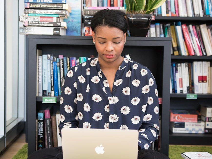 woman sits on floor facing gold macbook