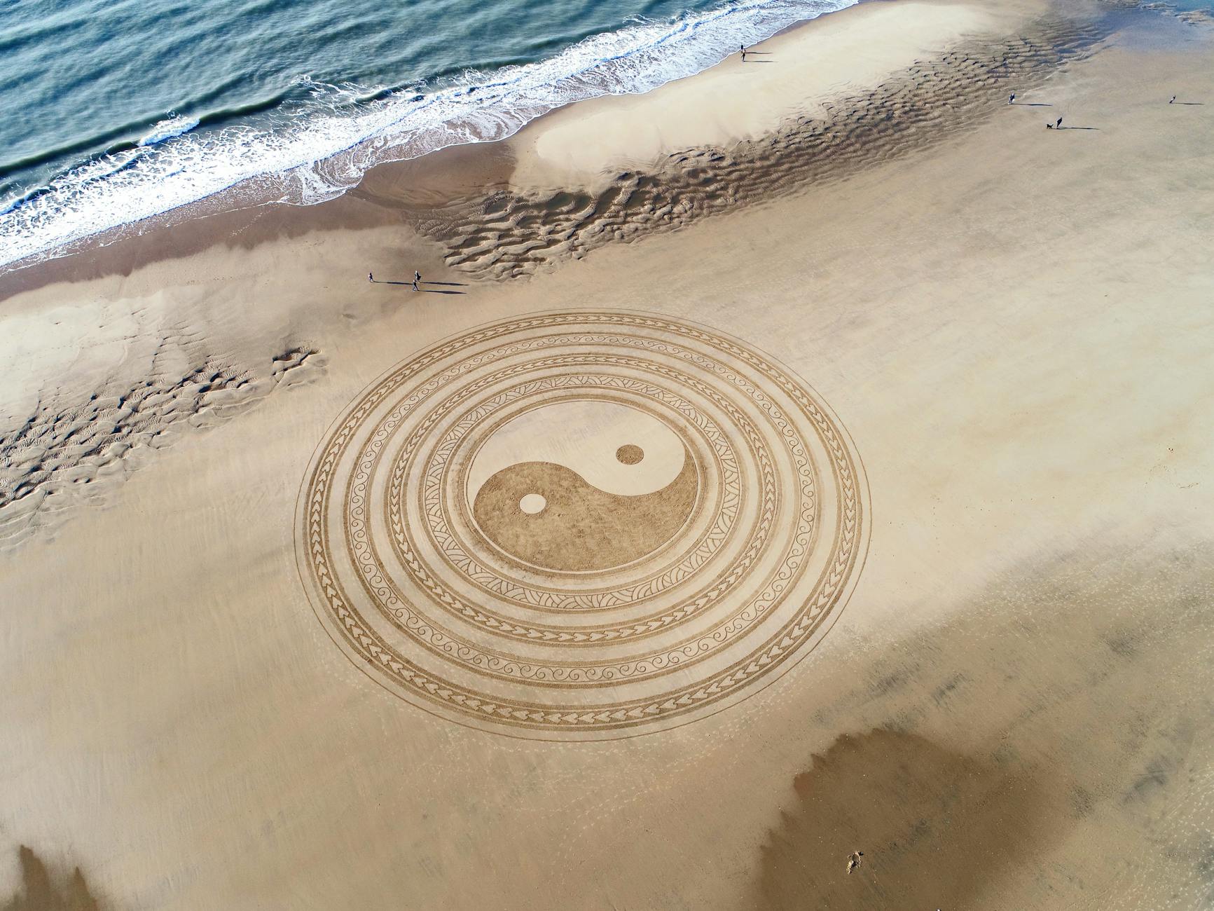 yin yang symbol on brown beach sand, evoking: lost wisdom of the zodiac, Hellenistic astrology, and ancient astrology
