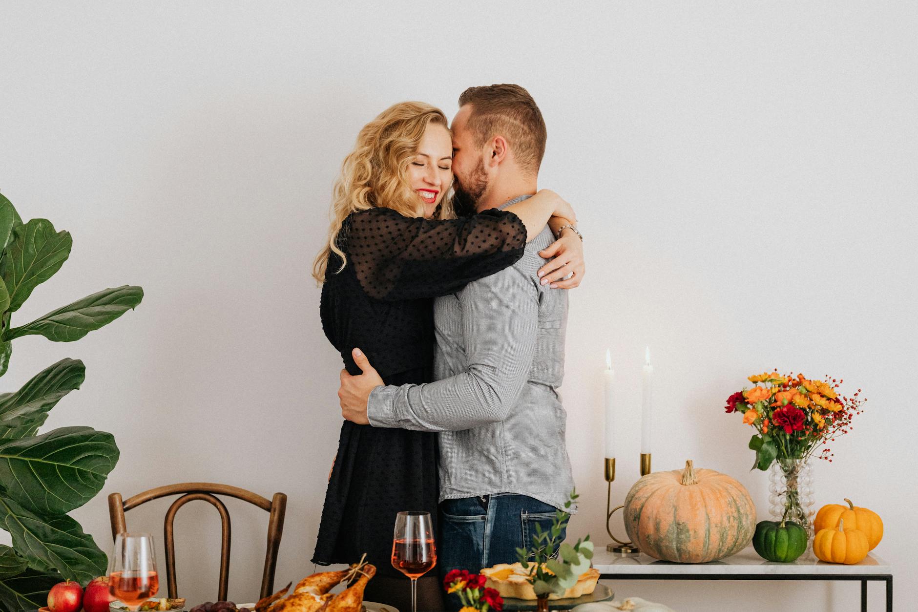 happy couple embracing and dinner on table, illustrating: holidays, rituals, holiday ritual, seasonal tradition, and traditions