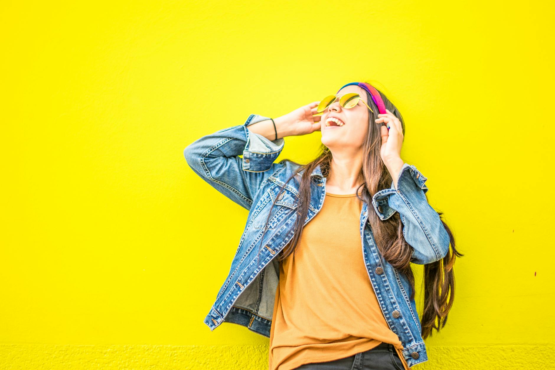 smiling woman looking upright standing against yellow wall, evoking: real manifestation, gratitude, abundance mindset, and intentional living