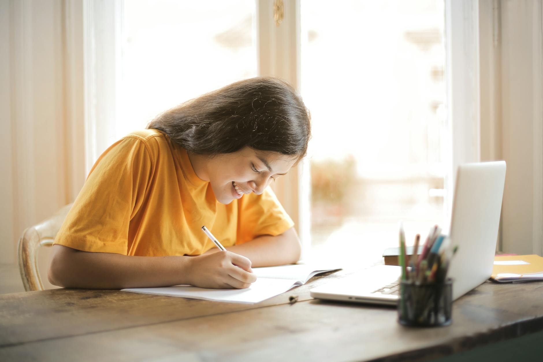 woman in yellow shirt writing on white paper, evoking: Year and a Day, Witches' New Year, devotional practice, spiritual commitment, and spiritual growth