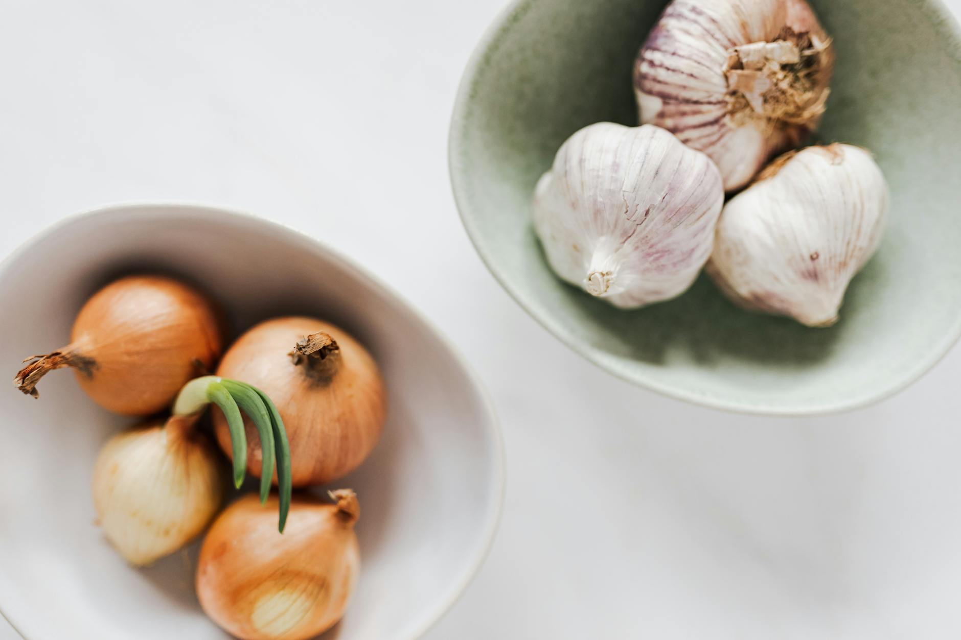 bowls of garlic heads and onions on white table, illustrating: Samhain, Harvest Season, Stew Recipe, Nourishing Dish, and a Samhain Feast