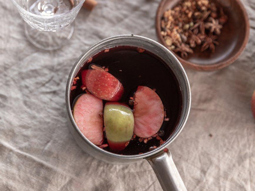 slices of apples floating on a red liquid, evoking: a Samhain wassail recipe, warm mulled cider, Samhain ritual drink, harvest blessing wassail, and an ancestors Samhain toast