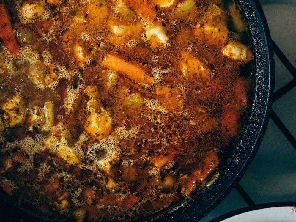 appetizing vegetable soup in saucepan placed on stove, illustrating: Samhain, Harvest Season, Stew Recipe, Nourishing Dish, and a Samhain Feast