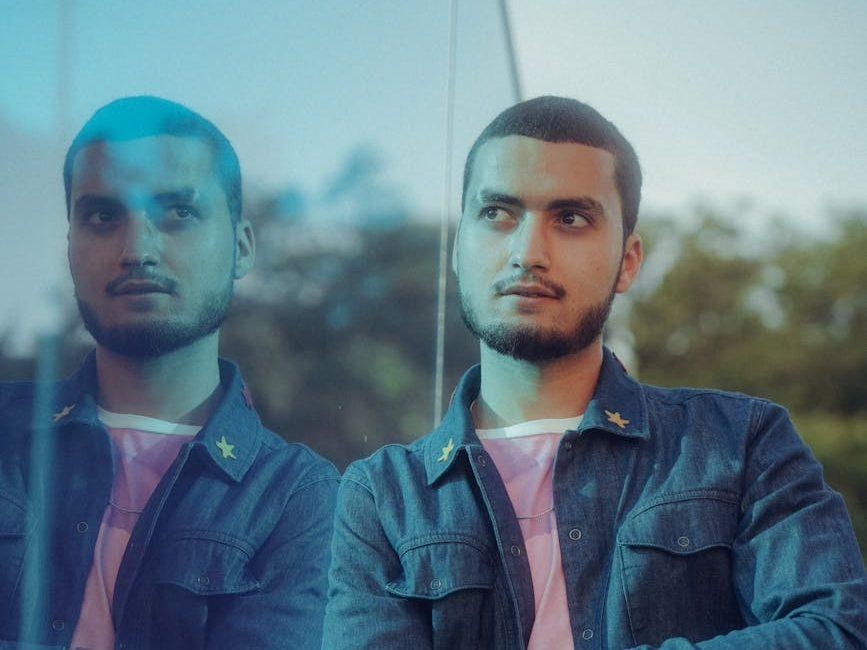 a man in a blue shirt and jeans standing in front of a mirror