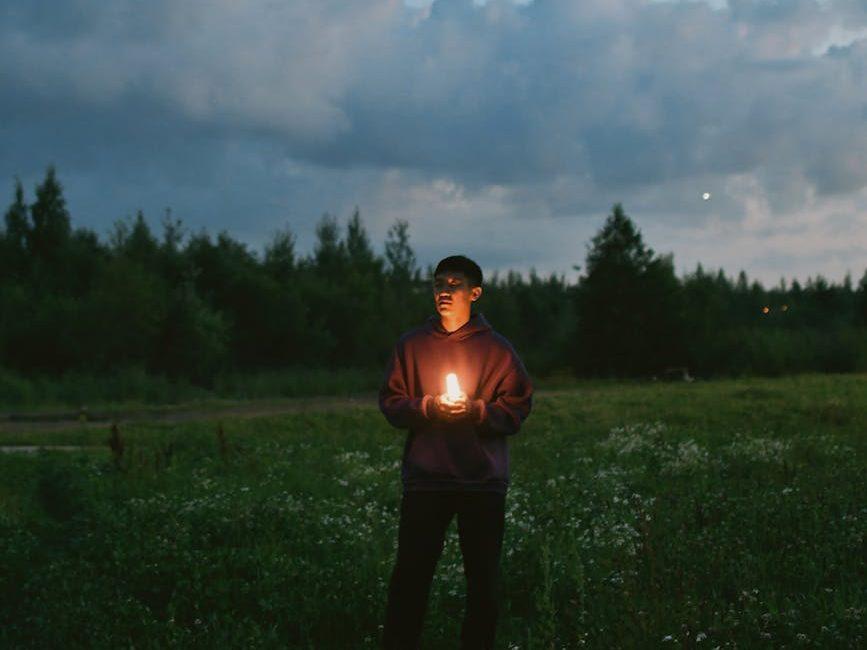 young man standing in a meadow with a glowing stick in hands at dusk, evoking: Sagittarius, Sagittarius season, Hellenistic astrology, Zodiac, and wisdom