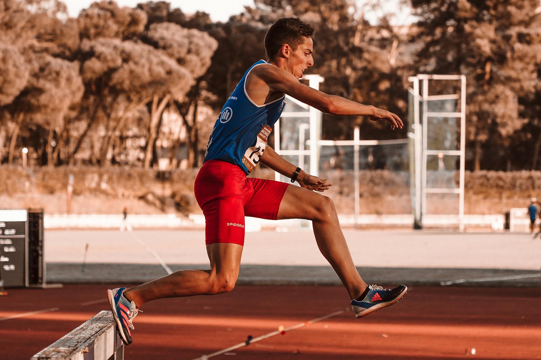man in blue tank top and red shorts on track and field