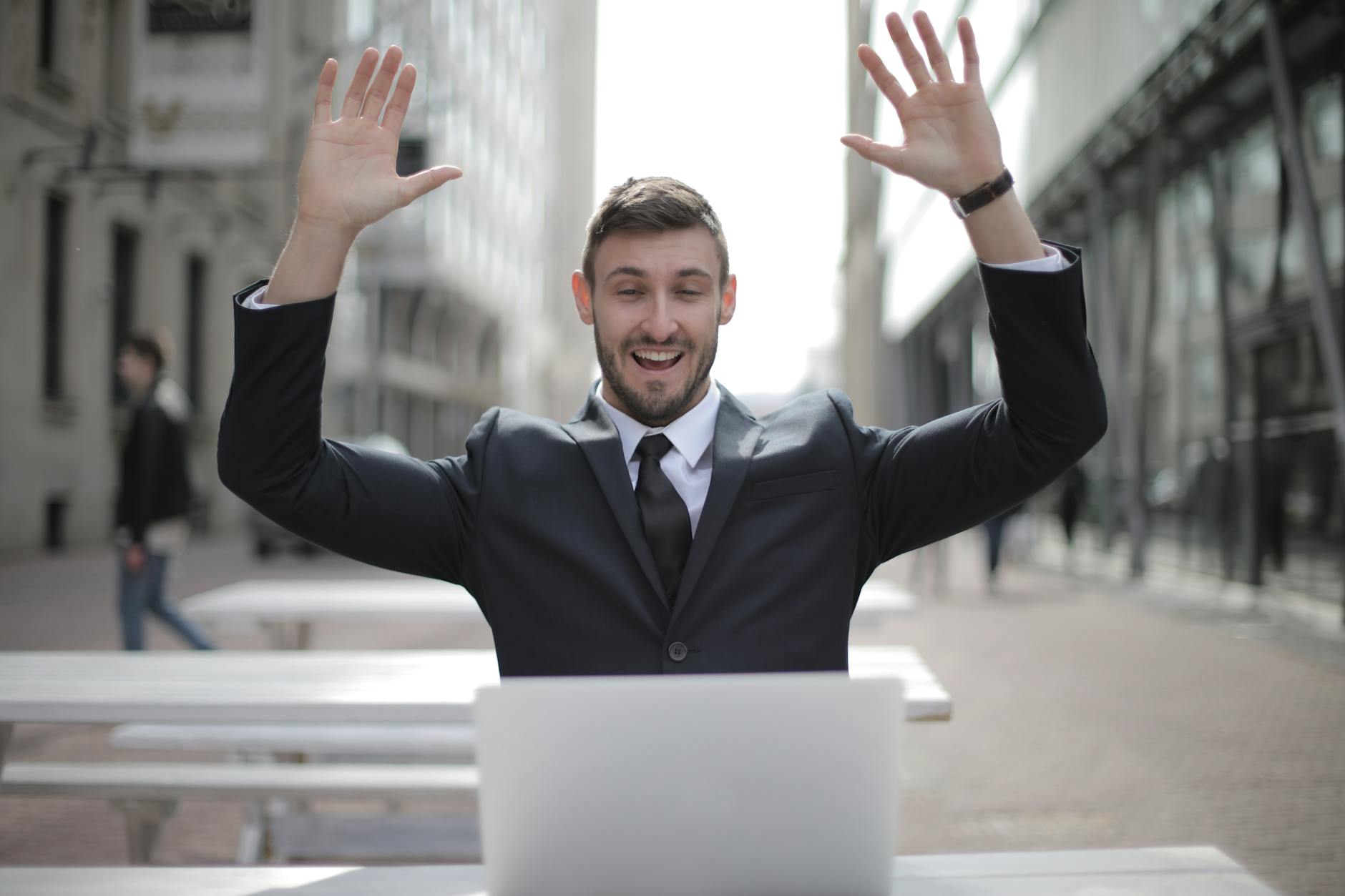 man in black suit raising both hands in front of his computer, expressing his joy about the benefits of his Onesce Insider spiritual growth membership