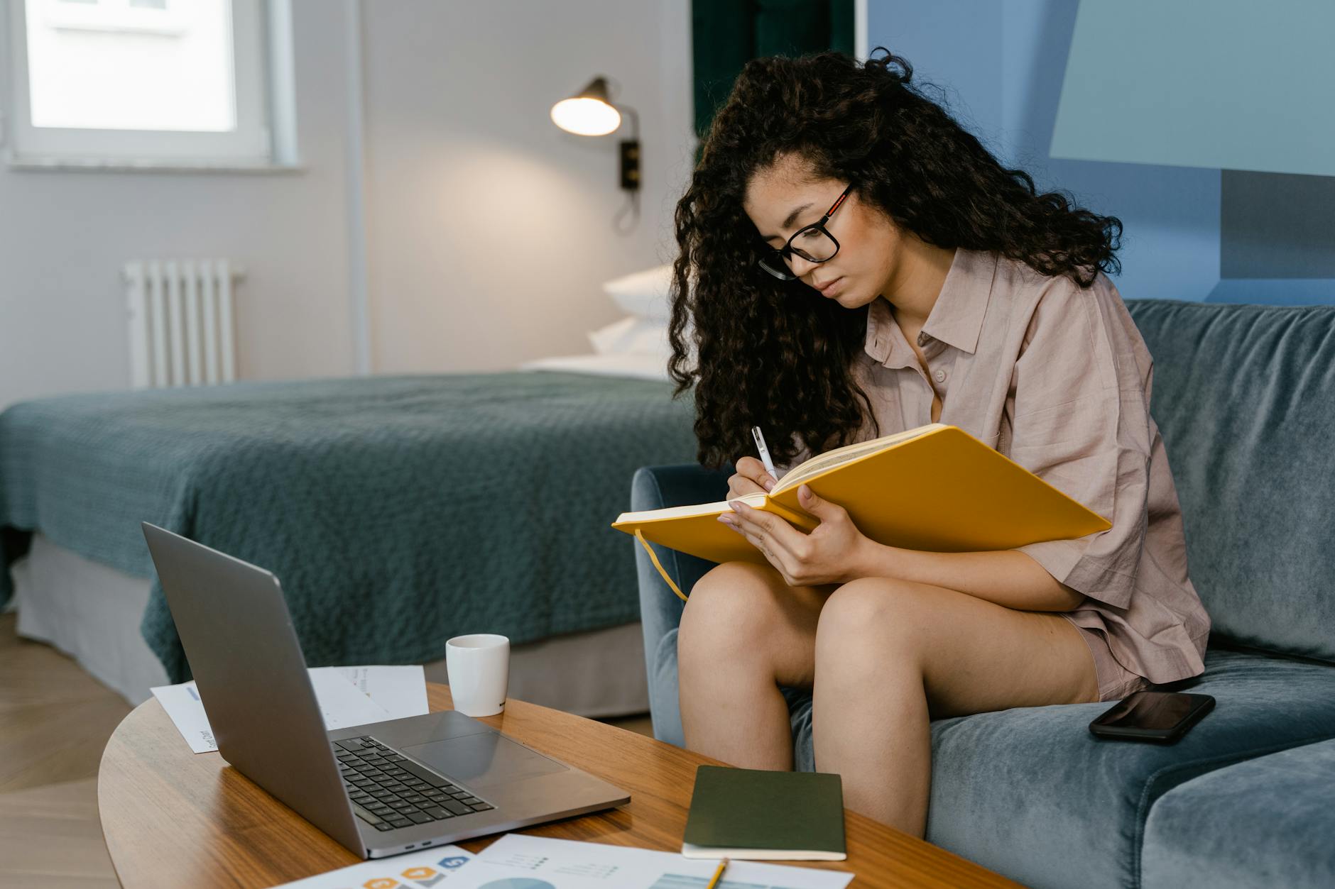 a young woman writing in a notebook while sitting on a couch, evoking: Capricorn, winter solstice, zodiac, astrological sign, and the solar cycle