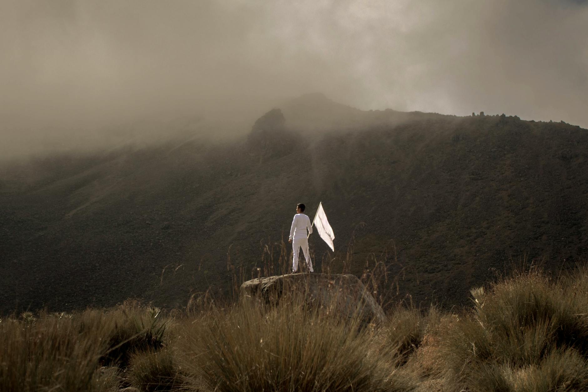 person with white flag standing on rock near nevado de toluca in mexico, illustrating surrendering control