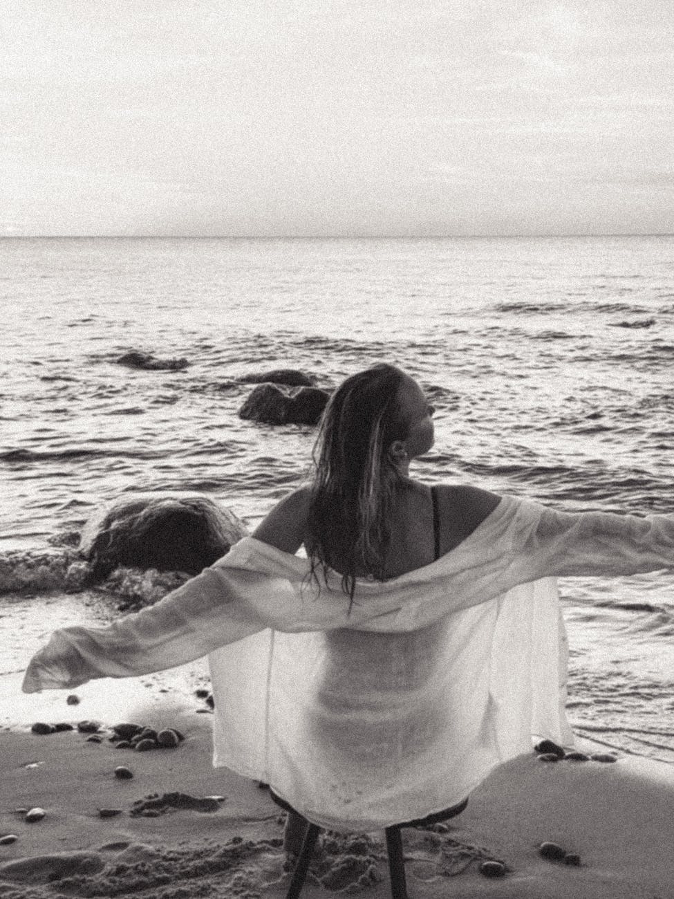 a woman sitting on the beach with her arms outstretched, illustrating letting go in meditation practice