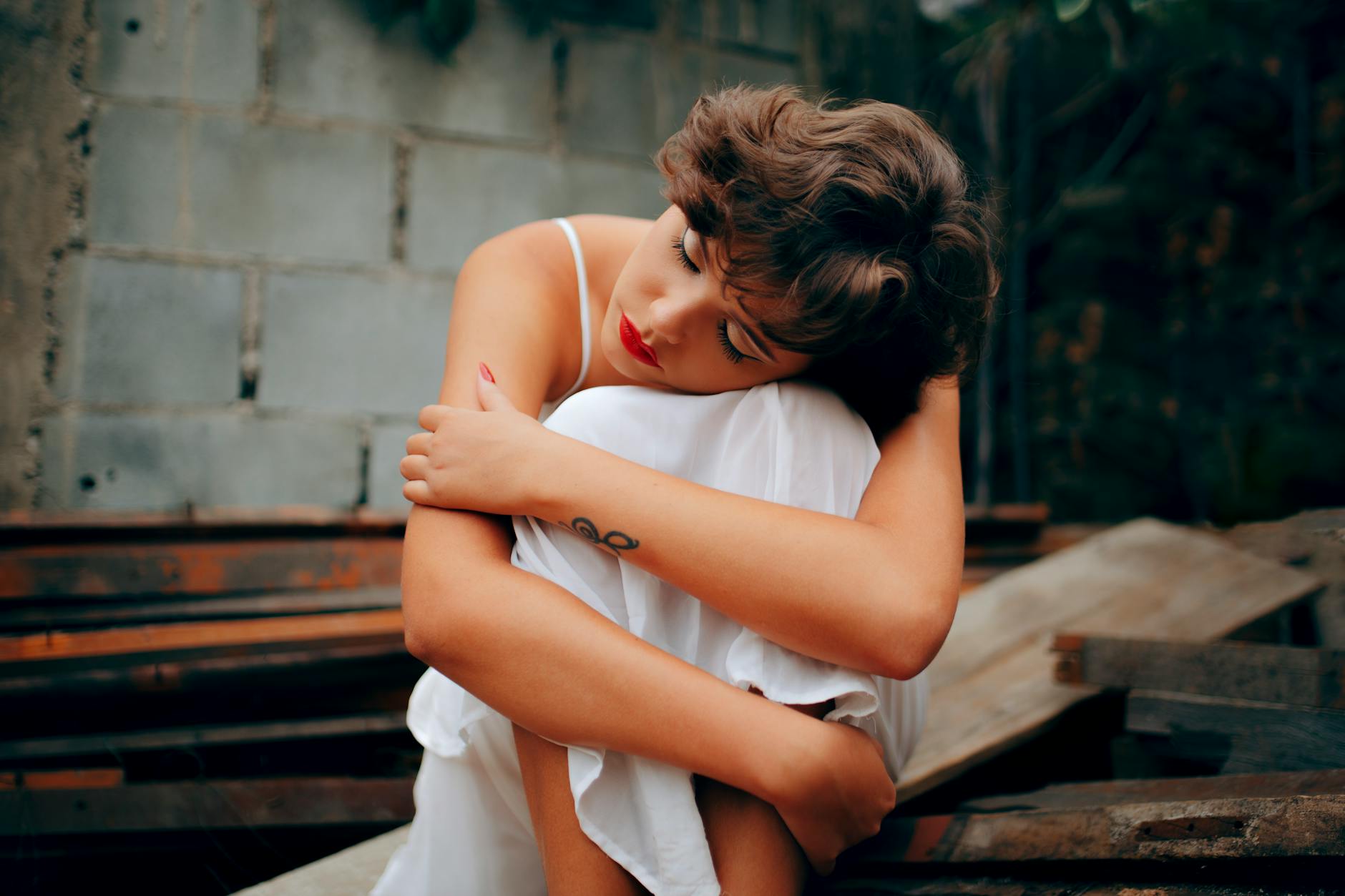 woman squatting near gray concrete wall, huggin herself with self-compassion for emotional healing