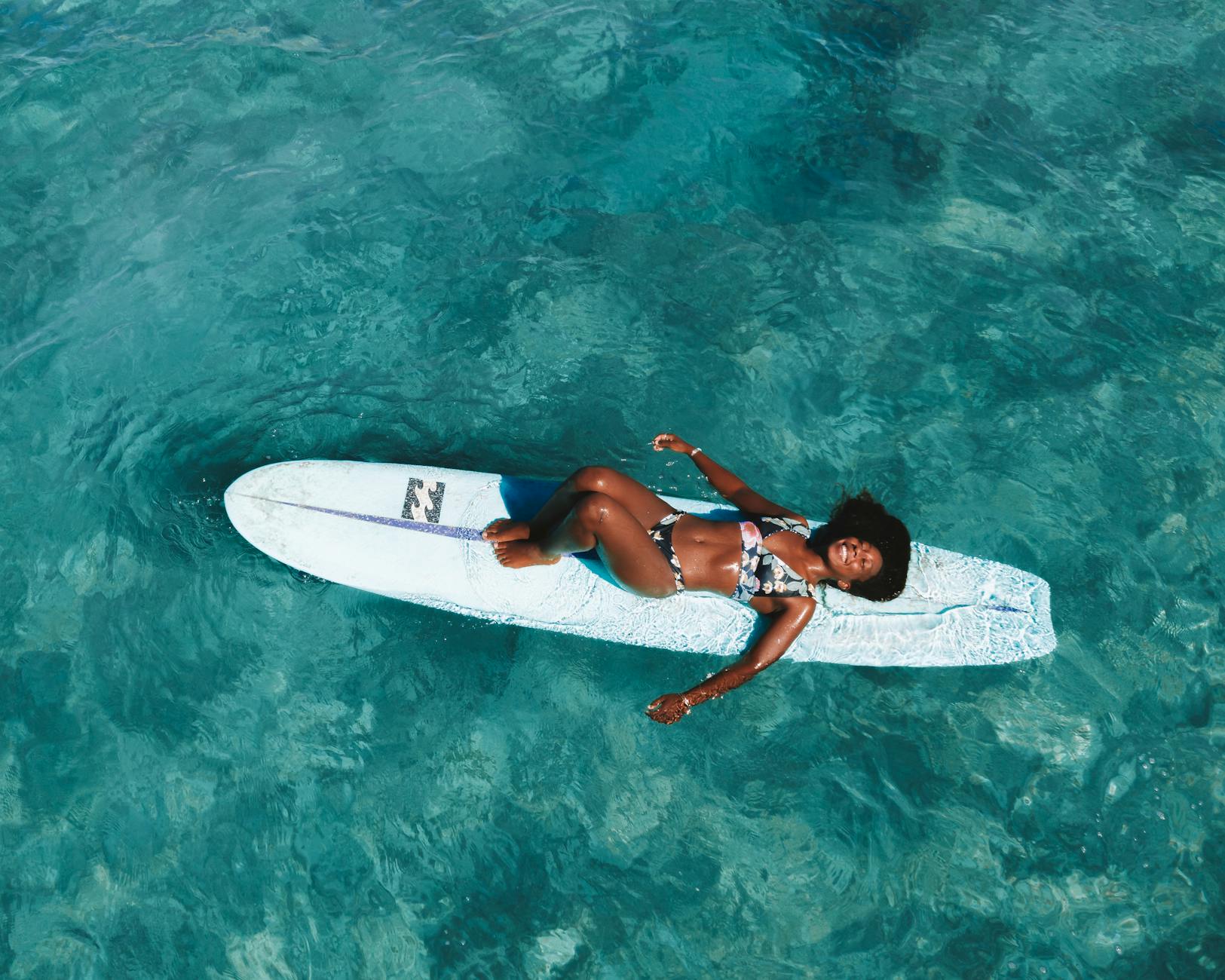 photo of a woman in a floral bikini lying on a blue surfboard, practicing self-compassion for emotional healing and self-care