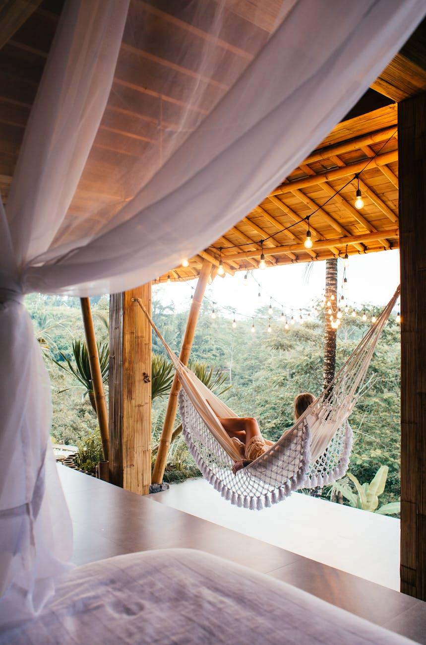 unrecognizable traveler in hammock against bed in tropical resort, illustrating the lunar rulership of the zodiac sign cancer, its connection to the summer solstice in the wheel of the year, and its cardinal water qualities per Hellenistic astrology