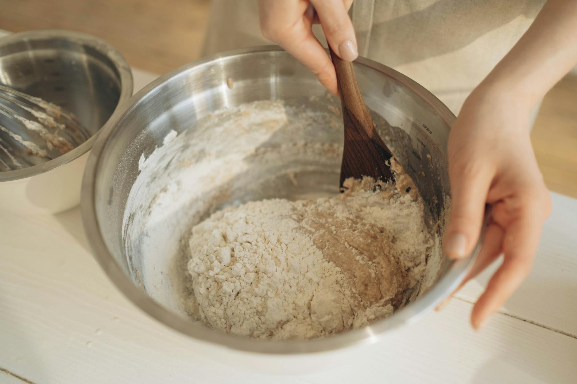 a person mixing the dough using a wooden spatula in a stainless bowl, making sunflower seed bread, a Litha recipe for celebrating Litha as a kitchen witch