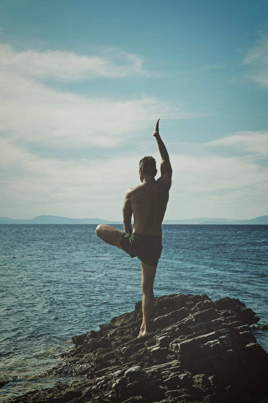 topless man standing on rock formation using right leg only, exploring meditation style, personalized meditation, traditional meditation, mindfulness habits, and mind-body connection