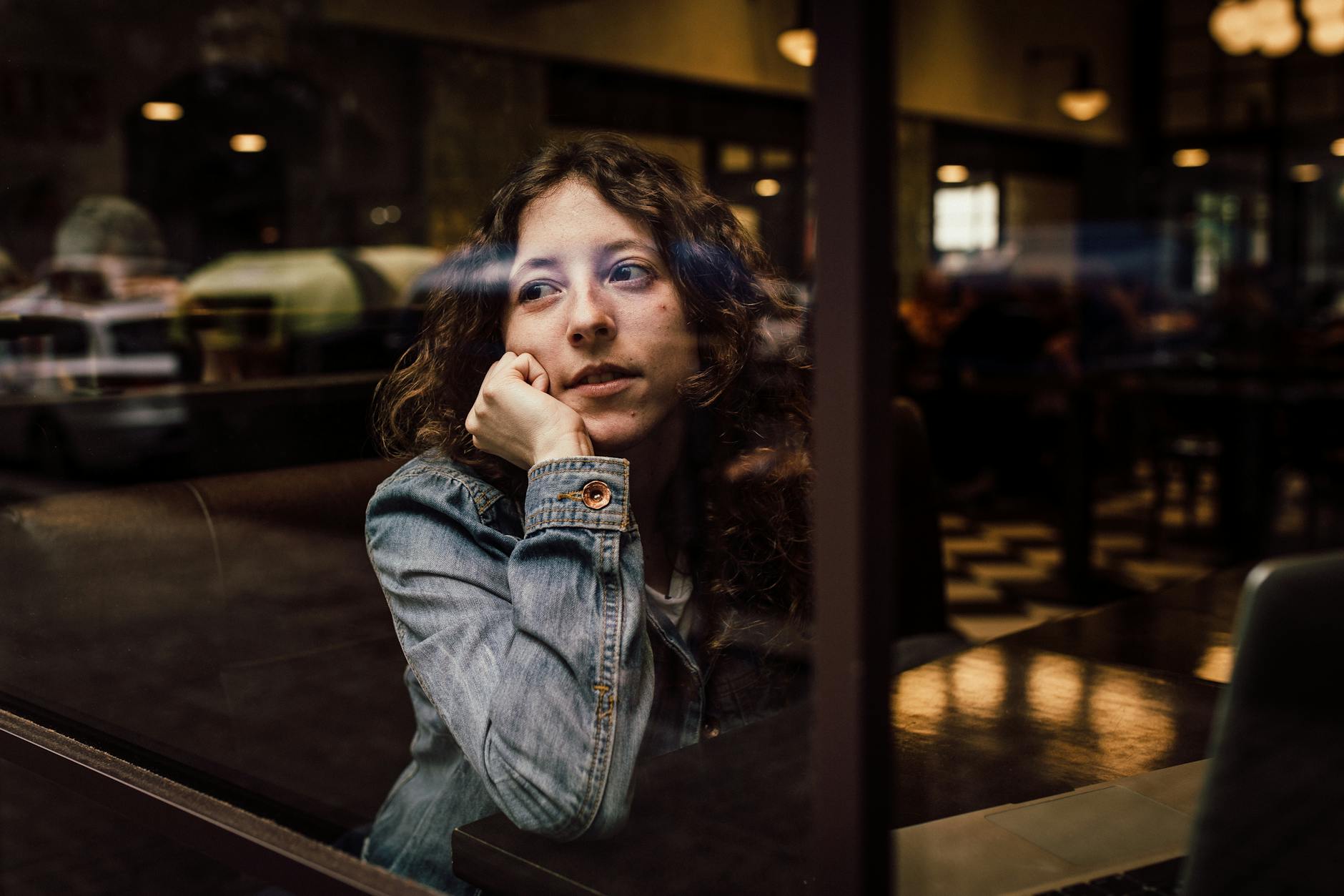 woman wearing blue denim jacket putting her right arm on her cheek, contemplating meditation for daily life, mindfulness routines, daily meditation practice, mindfulness habits, and how to integrate meditation
