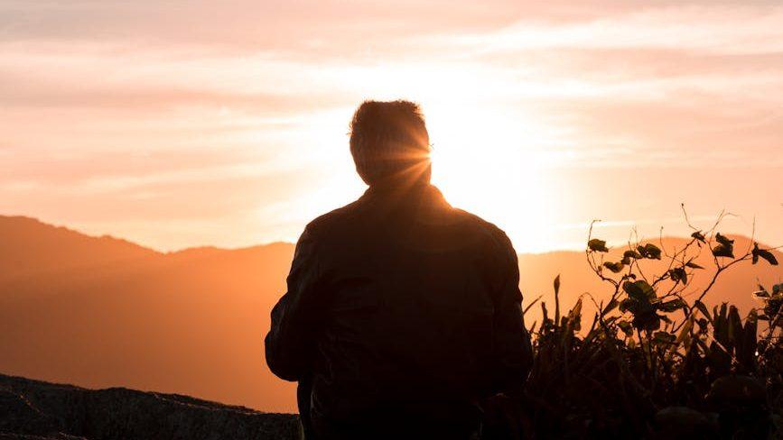 silhouette of person sitting and facing mountain during sunset, considering meditation hurdles, consistent practice, sustain mindfulness, meditation obstacles, and how to meditate consistently.