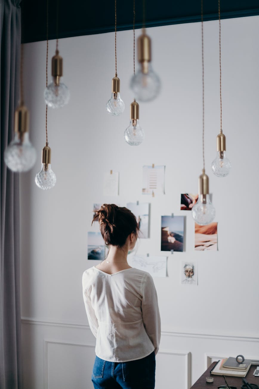 woman under pendant lights looking at the photo on the wall, considering harvest reflections, tarot spread, first harvest celebration, seasonal self-inquiry, and summer sabbat ritual
