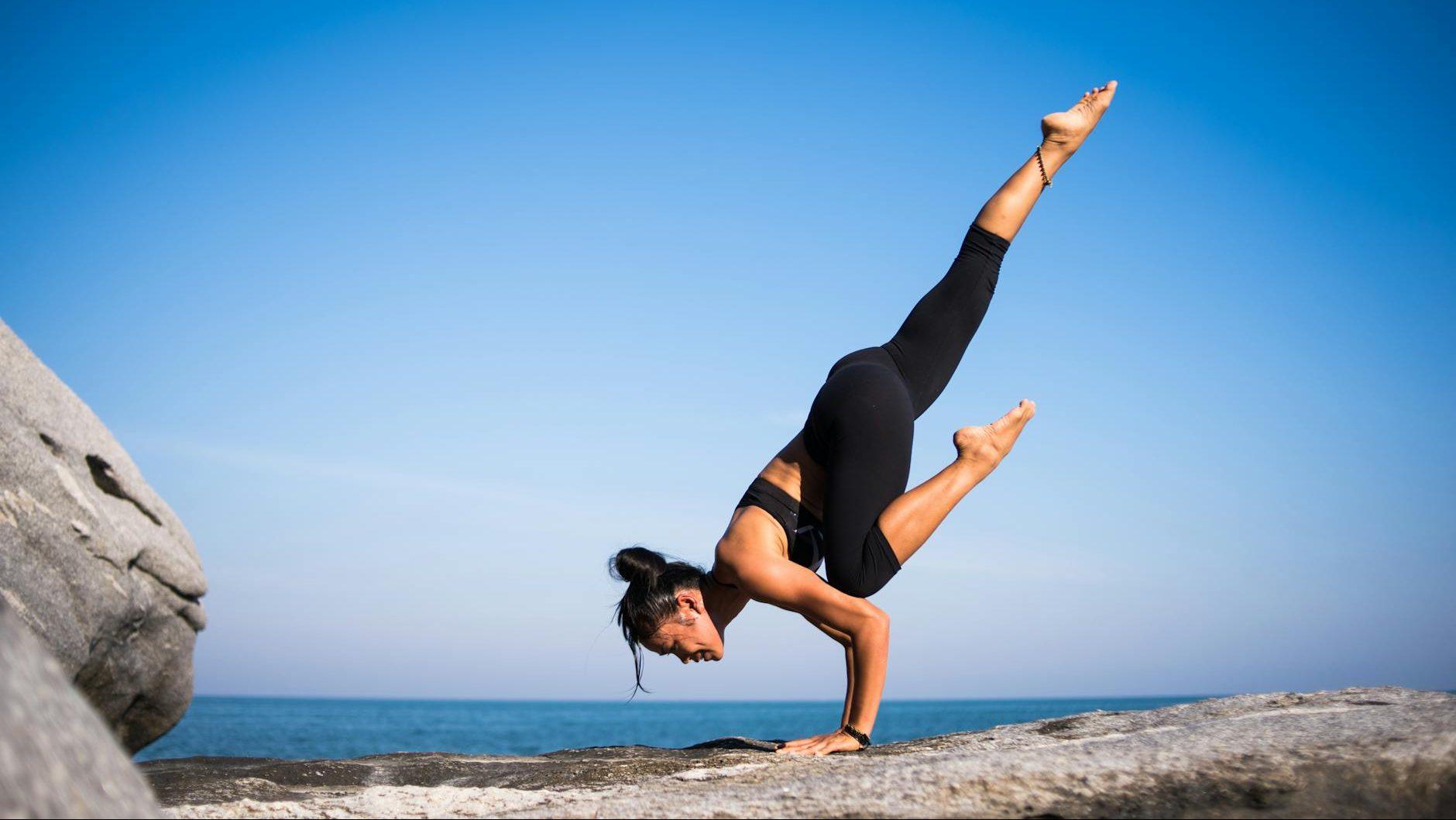 low angle view of woman relaxing on beach against blue sky, illustrating lasting wellbeing, benefits of meditation, stress relief, emotional resilience, and mind-body connection