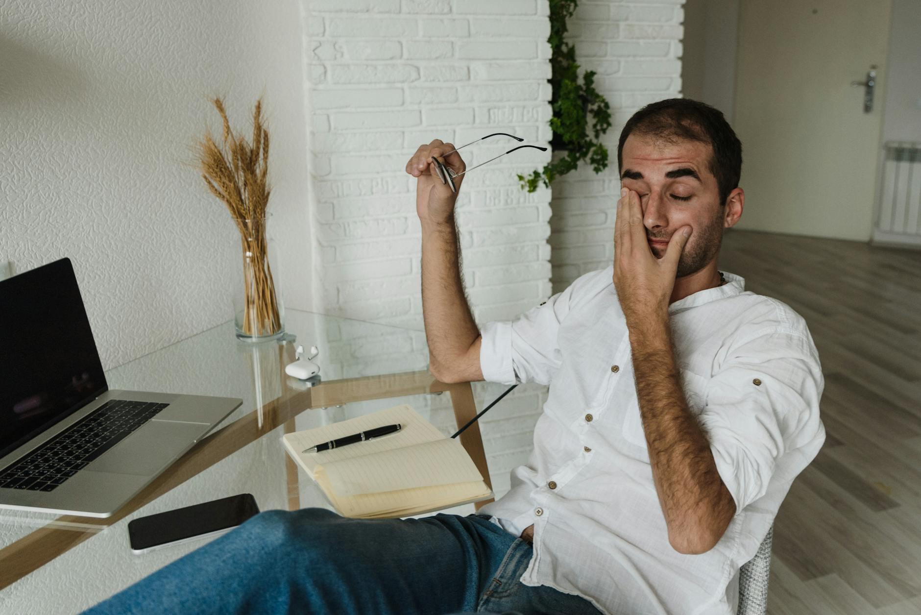 man in white dress shirt sitting on chair wiping eyes, illustrating lasting wellbeing, benefits of meditation, stress relief, emotional resilience, and mind-body connection